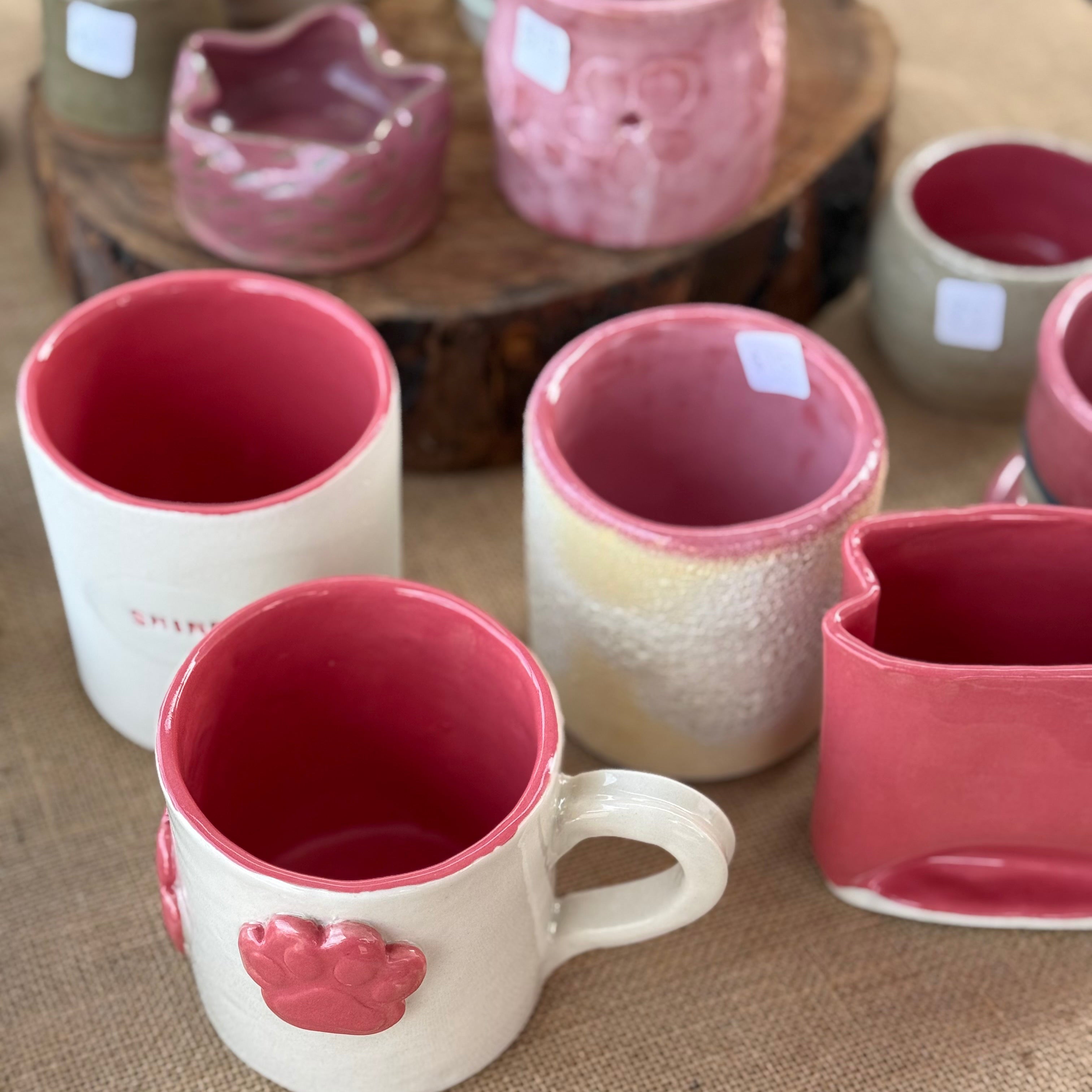 Collection of ceramic mugs and bowls with red interior on a textured surface.