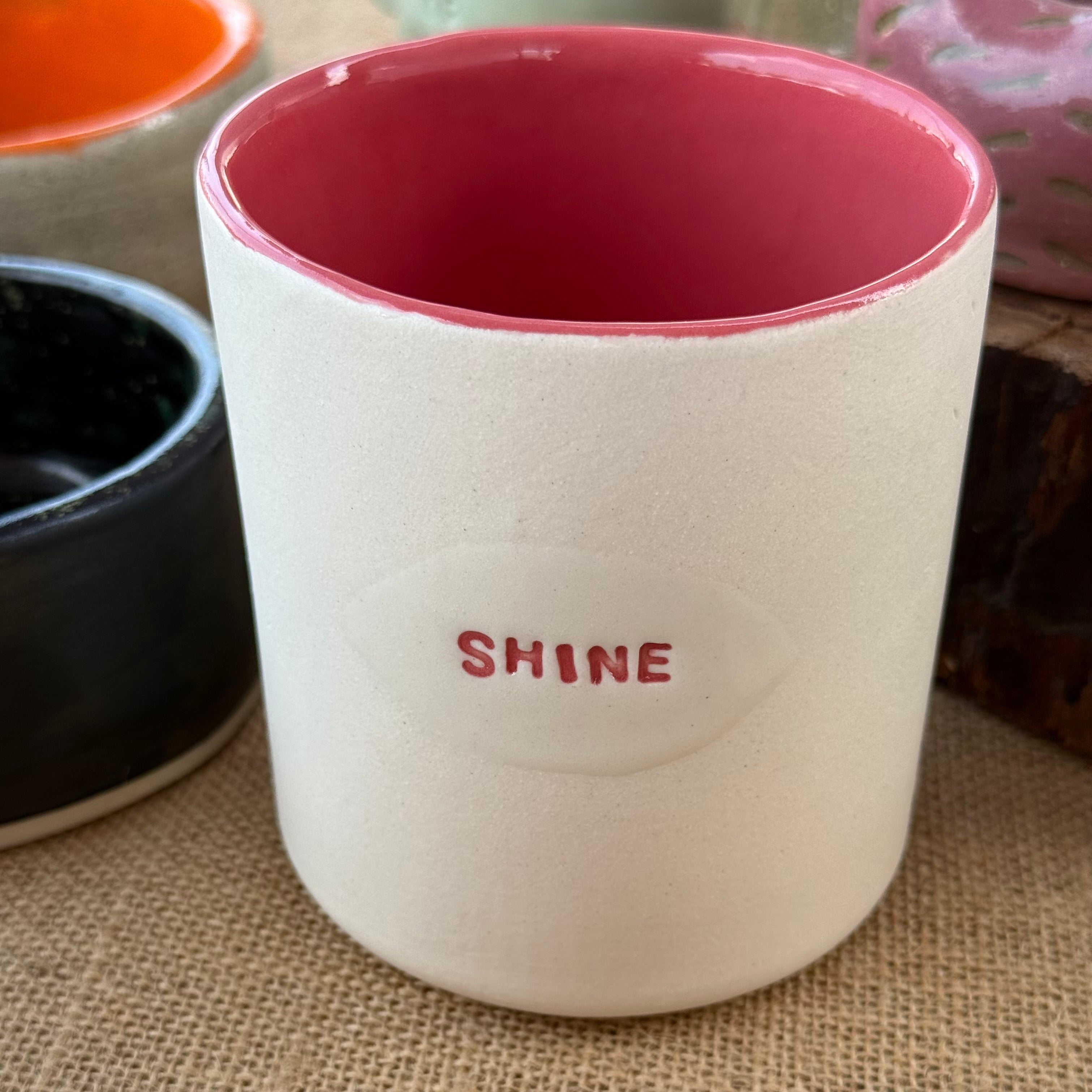White ceramic cup with red interior and 'SHINE' text on a textured surface